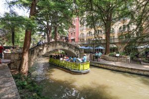 A charming bridge over the San Antonio River Walk with a yellow boat cruising underneath.