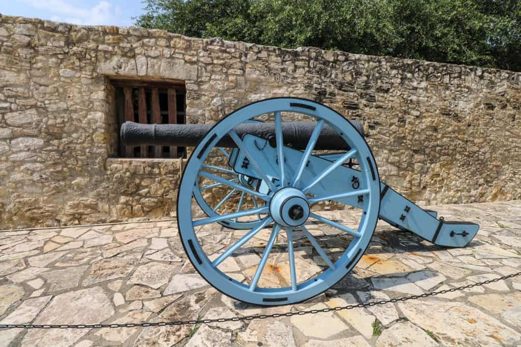 An old cannon on a light blue support with wheels in front of the Alamo and one of the top things to see on a weekend in San Antonio.