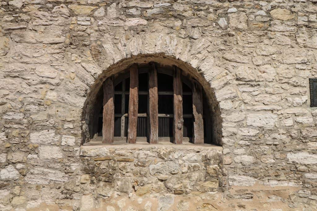 A small wooden half circle shaped window within the stone along the outside of the Alamo.