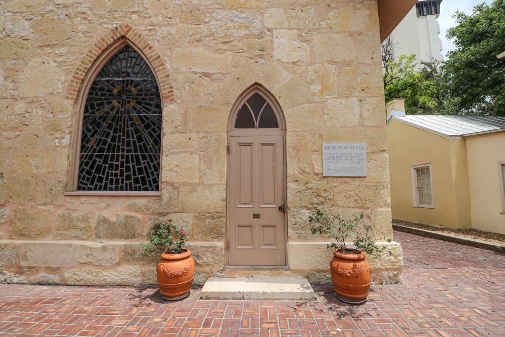 A charming door and window of a church that both have a pointed top with two potted plants on each side of the door.