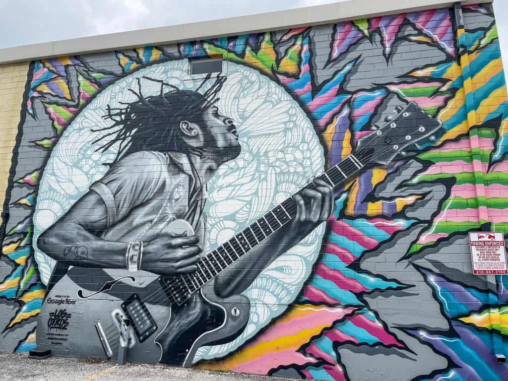 An art mural of a man playing on the guitar and bright colors surrounding him.
