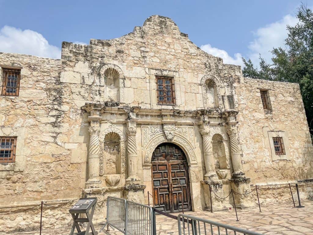 A close up front view of the Alamo made of limestone with a dark brown wooden door.