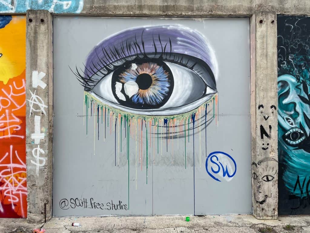 An art mural at Essex Modern City in San Antonio of an eye in colors of purple, gray and blue. The eye looks to be crying paint.