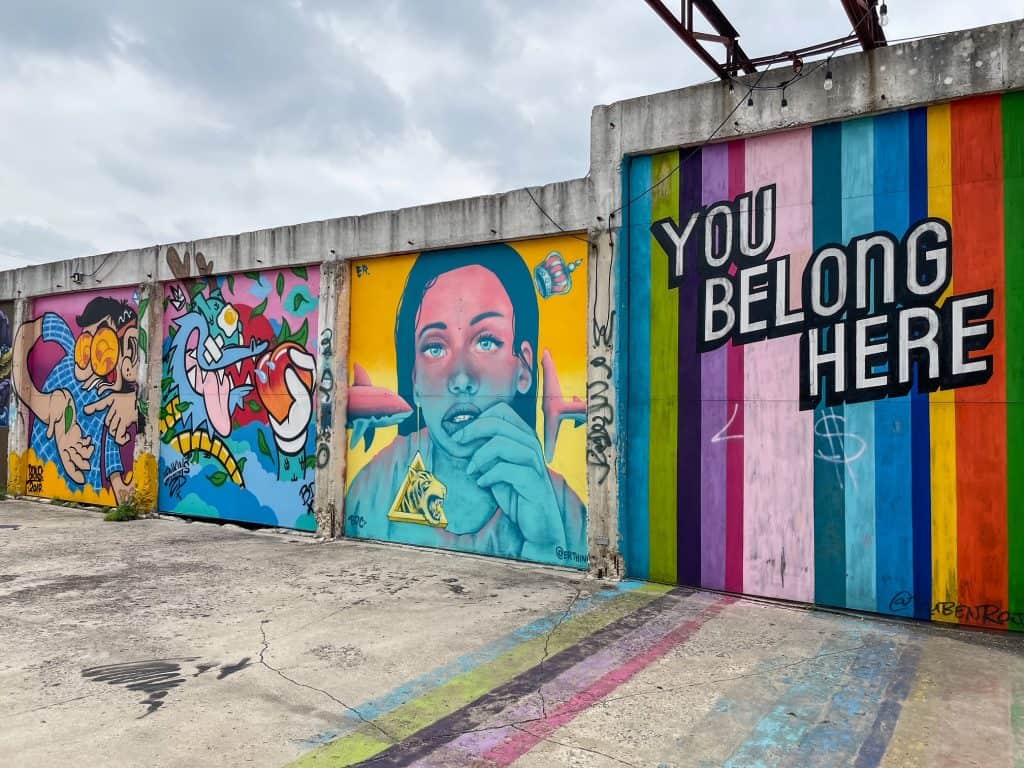 A vibrant series of art murals at Essex Modern City with one saying "You belong here" and a beautiful girl looking out in colors of blue and yellow.