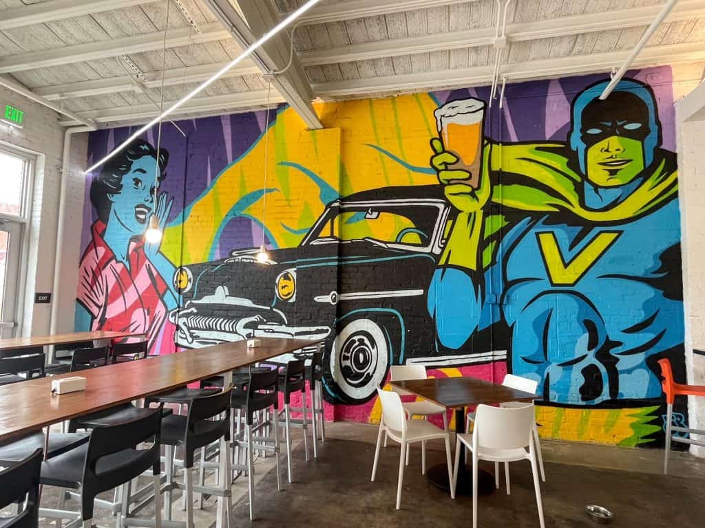 A fun and vibrant art mural inside Vanessa House Beer Co with a super hero holding up a beer.