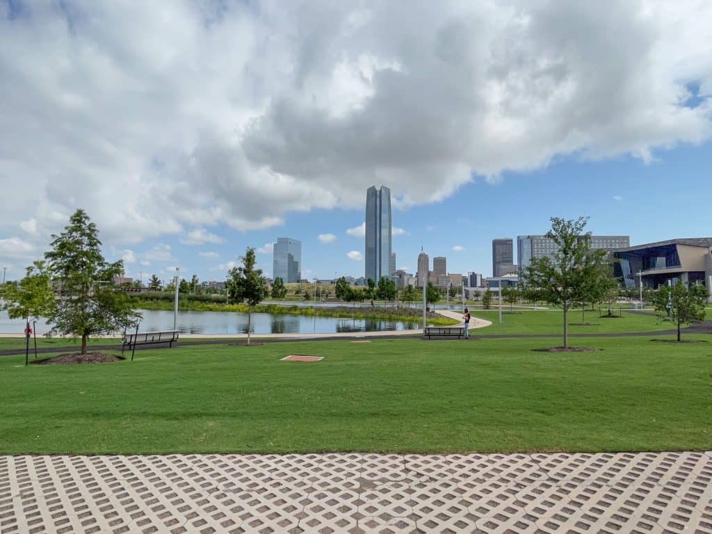 Looking across a huge lawn and the lake in Scissortail Park with city skyline in distance.