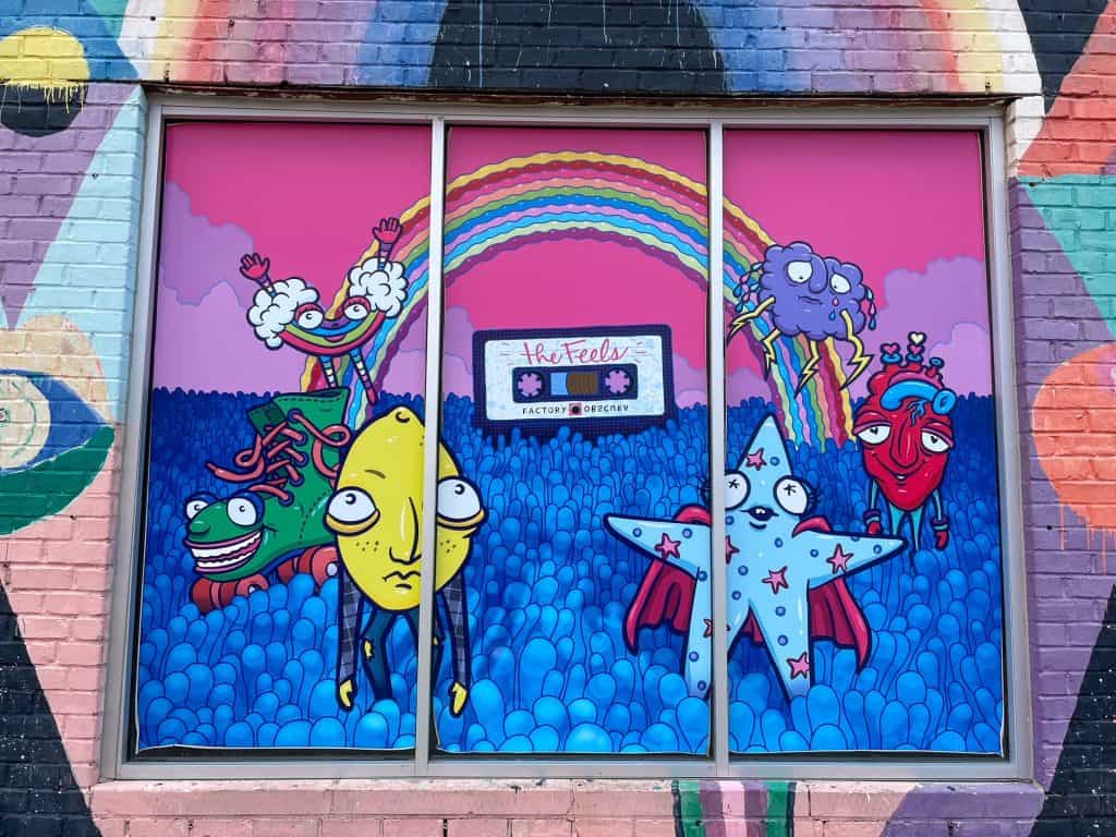 A very colorful art mural with cartoon like characters, a rainbow and an old cassette tape.
