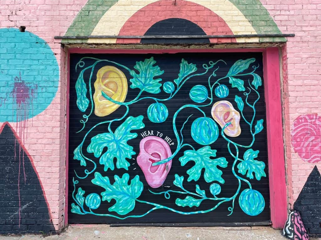 A black, turquoise and pink art mural with vines and a ear that says "hear to help".