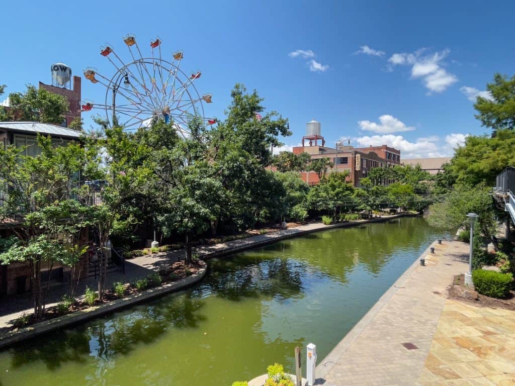 Walking along the river walk in Bricktown with a small Ferris Wheel in the background.
