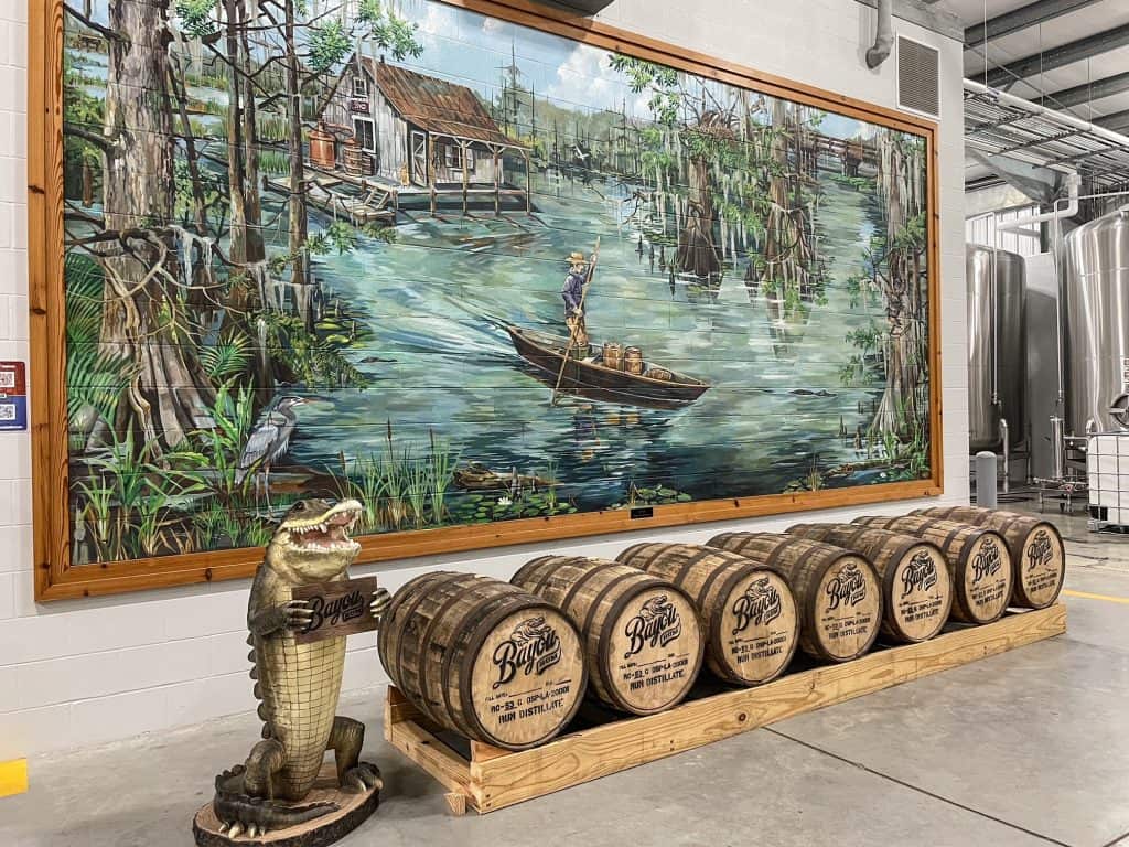 A colorful mural depicting life in the bayou, a fake alligator statue and a row of Bayou Rum casks at Bayou Rum Distillery.