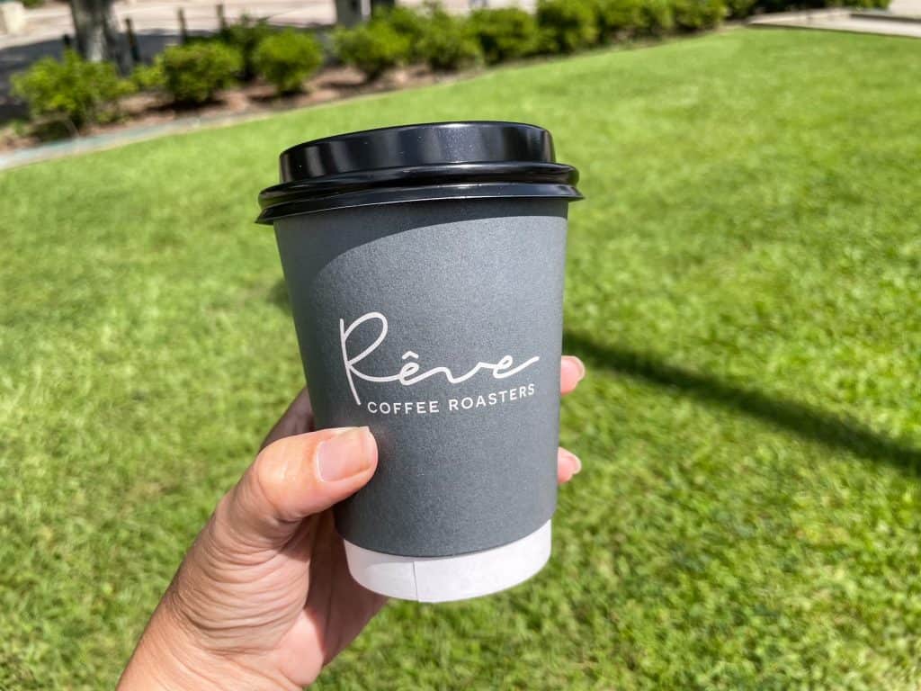 Holding a cup of coffee from Reve Coffee shop outside on a grassy area.