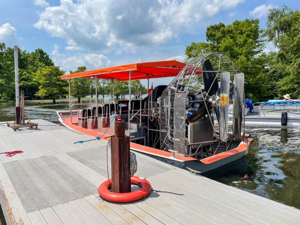 The airboat at the dock with a orange canopy that you take on the swamp tour.