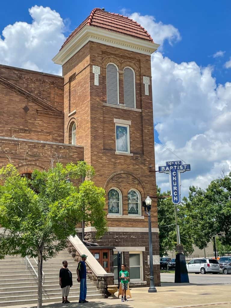 A vertical view of the end section of the Church and a vertical blue and white sign that says 16th Street Baptist Church.