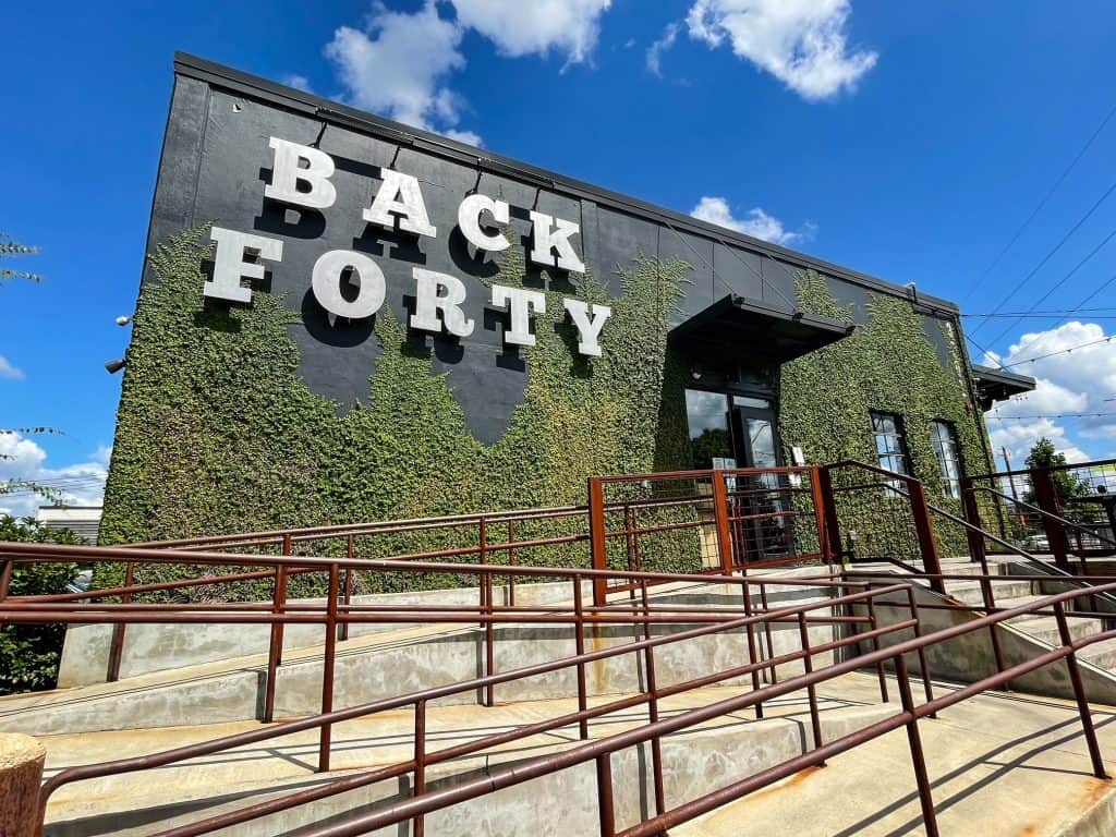 The front entrance of Back Forty Brewery that has a green moss covering the lower half of the black building and sign for Back Forty.
