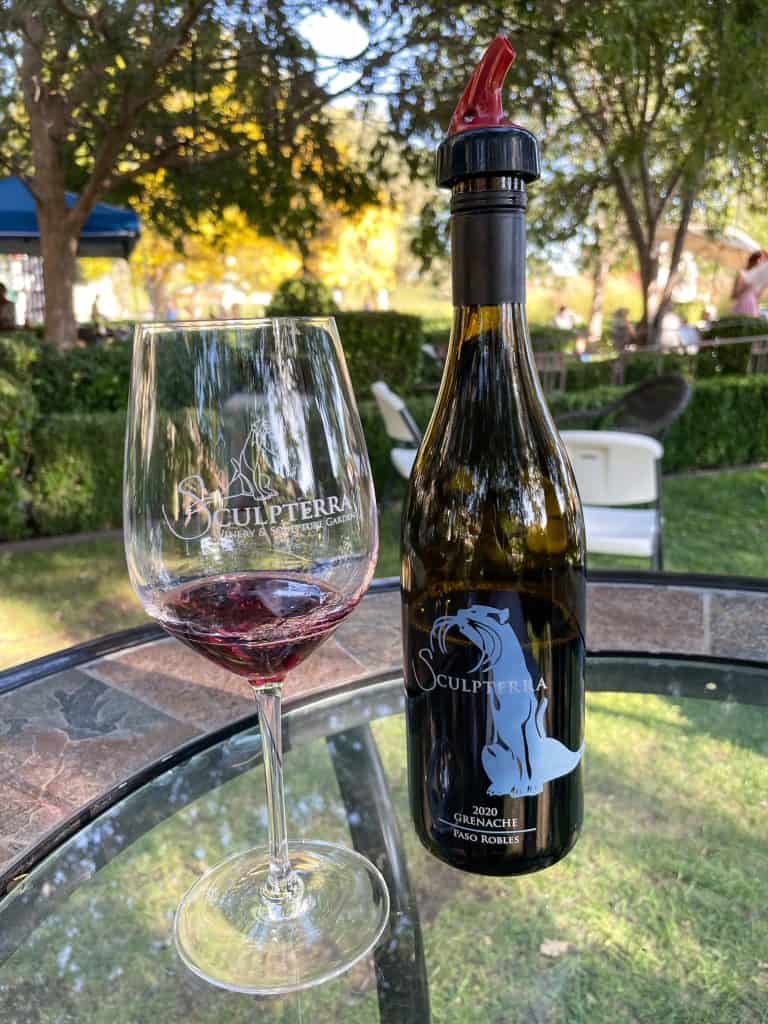 A glass of wine next to a bottle that has the logo the same as a big cat sculpture at the winery.