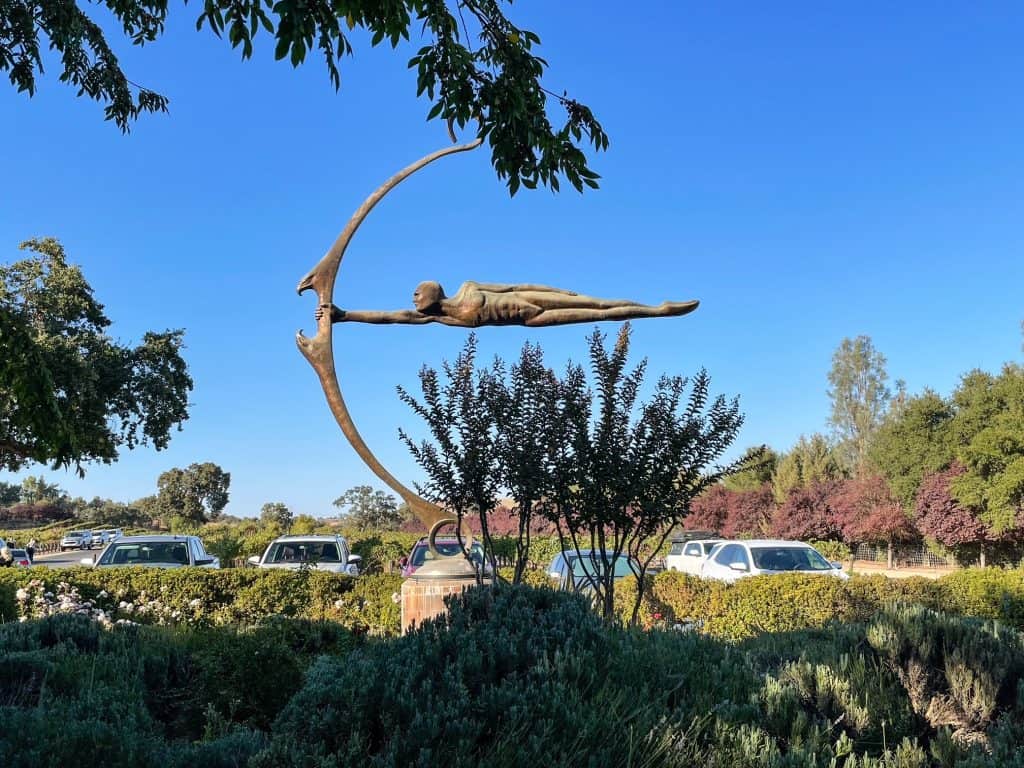 Sculpture of a person lying straight horizontally holding onto a bow.