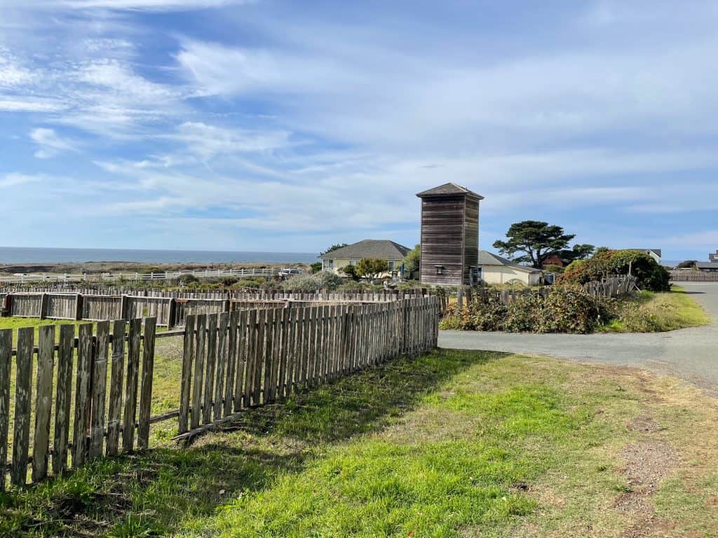Walking towards to coastal bluffs along a wooden fence and small water tower on a sunny day.