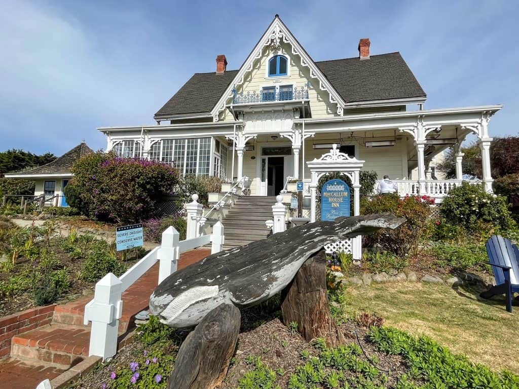 The elegant Victorian style MacCallum House in white and pale yellow with a wooden whale out front.