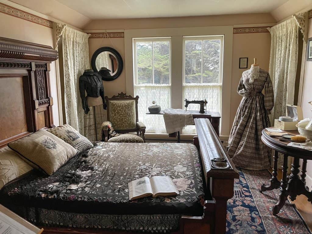 Inside the main bedroom at the Kelley House filled with antiques such as a bed and clothing.