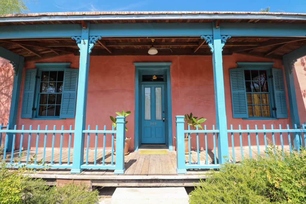 A pink adobe-style house with a porch and trim and railings painted in a light blue in the Barrio Viejo neighborhood of Tucson.