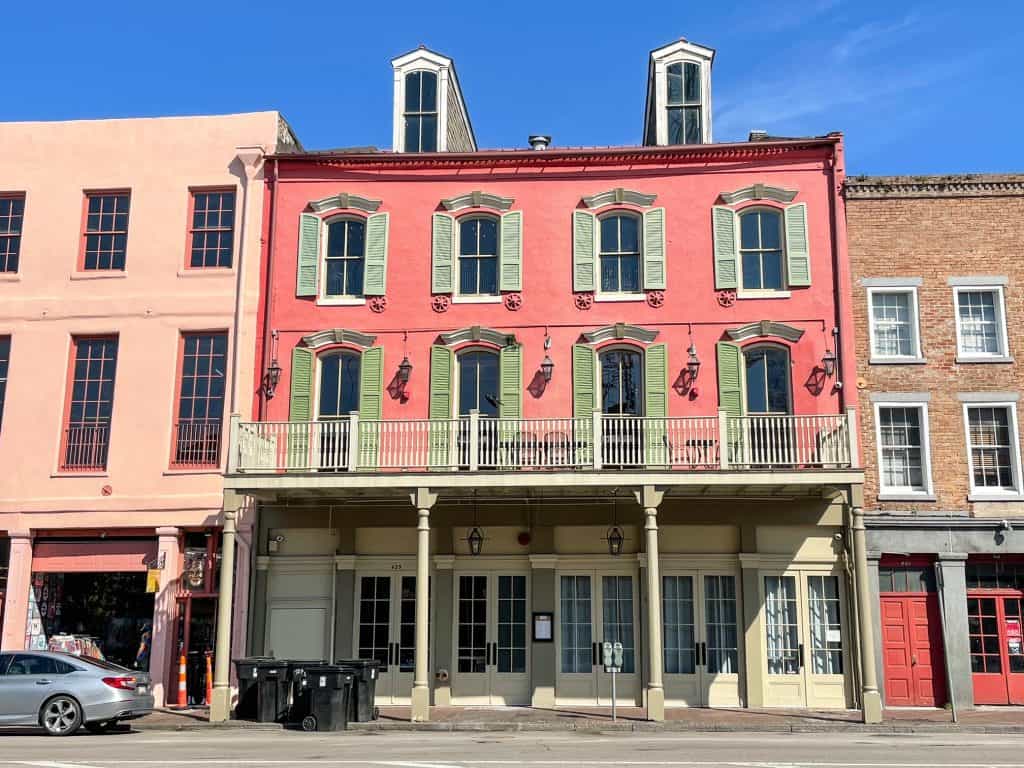 A dark pink building with pale green shutters in a classic French Quarter architecture.