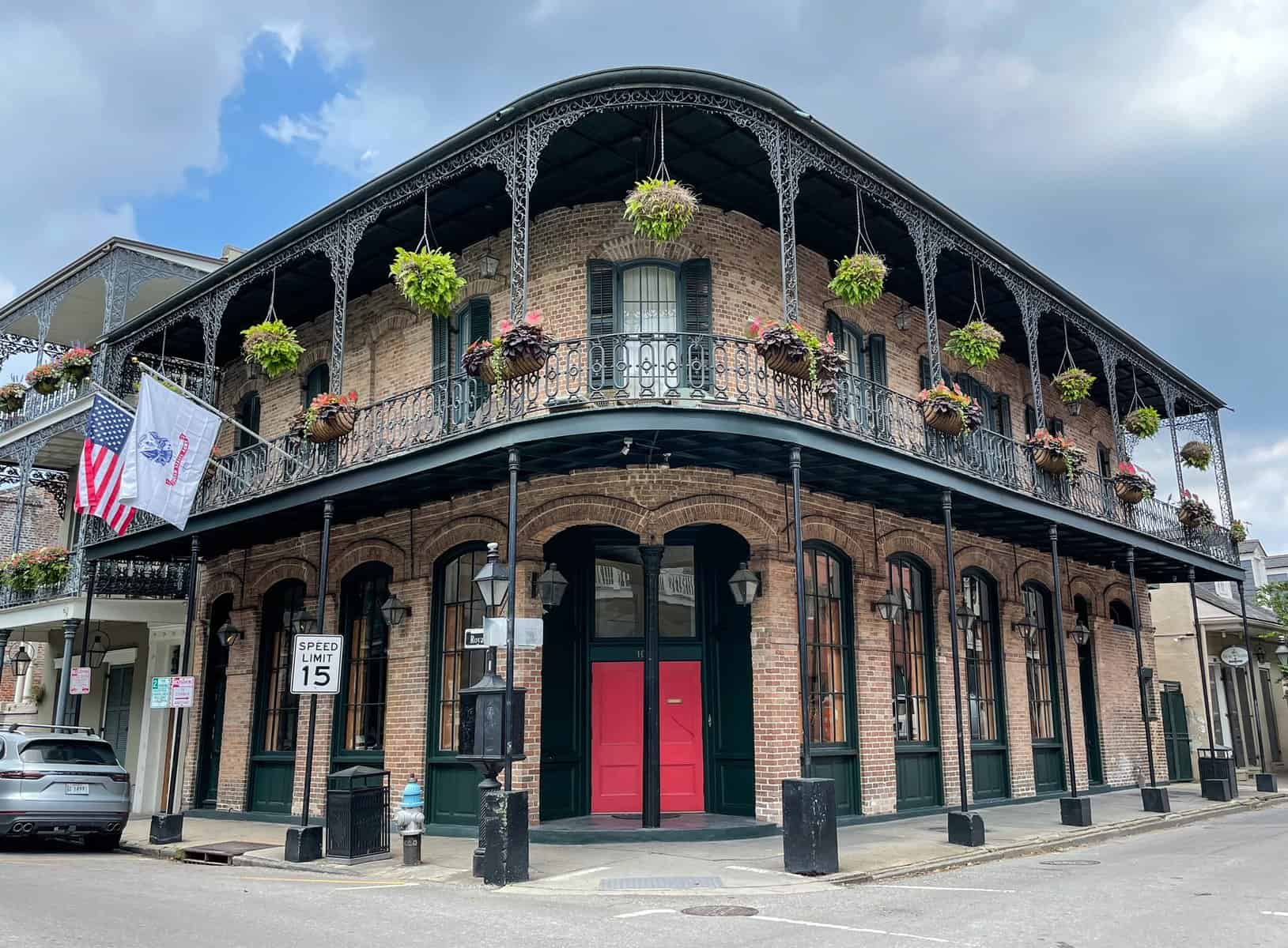 A classic 2-story building in the French Quarter of New Orleans with a balcony, hanging plants, and a bright red door.