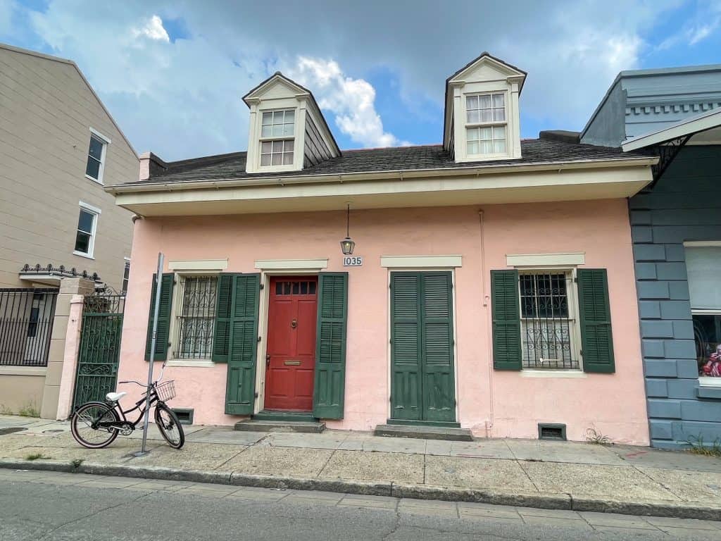 A charming pale pink house with dark green door and shutter with a bike in front in New Orleans.