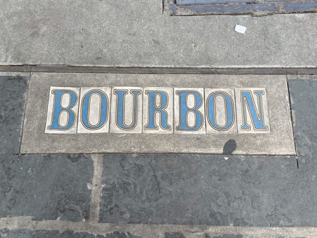 Tile blue and white letters that spell BOURBON on the the sidewalk.
