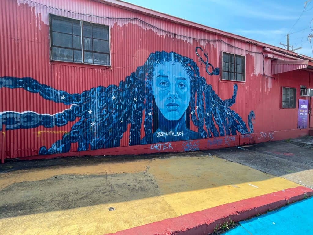 A pink and blue mural of a young girl with her hair flowing around her at Studio Be.