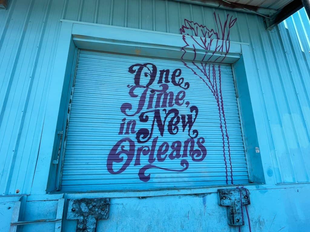 A beautiful art mural in blue with purple lettering "One time in New Orleans"., is a top things to do on this New Orleans bucket list.