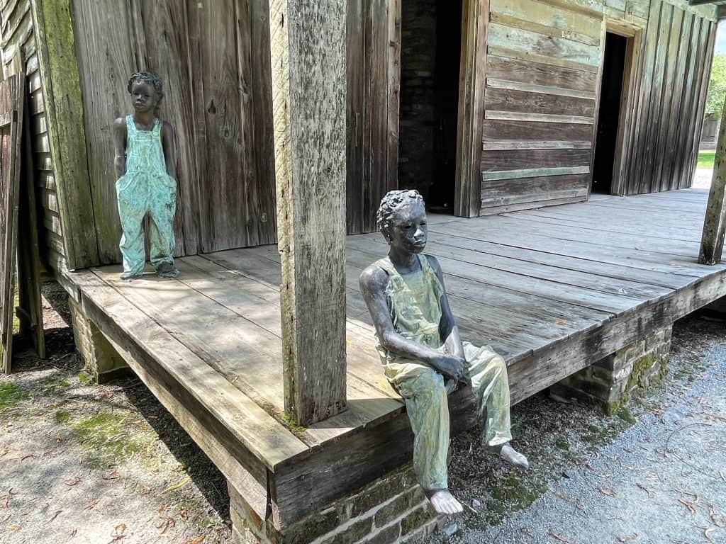 Two slave children statues sitting on the porch of a slave cabin.