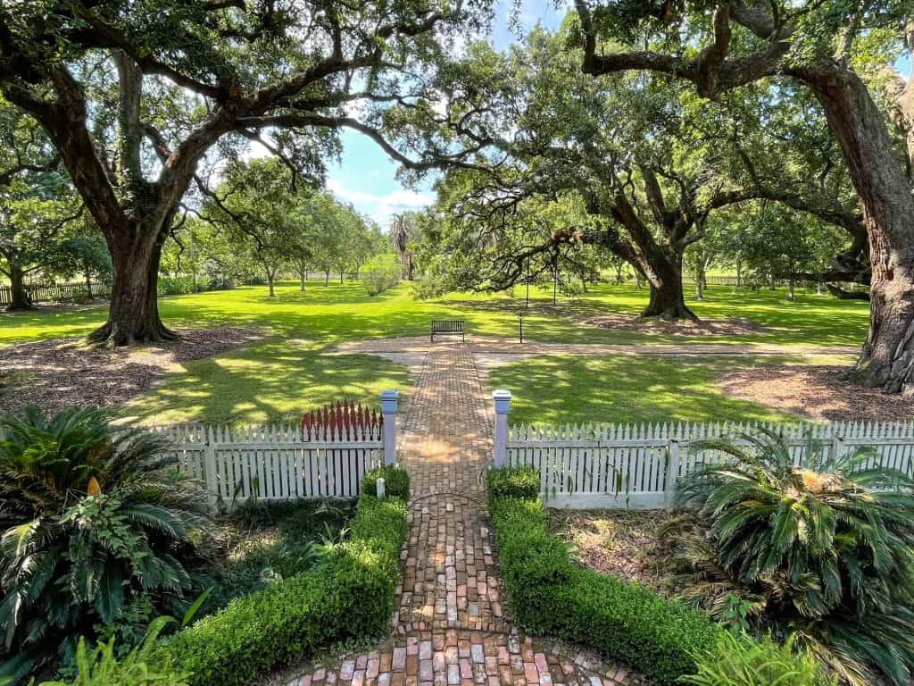 Looking out at the manicured garden, oak trees and a white picket fence at the Laura Plantation.