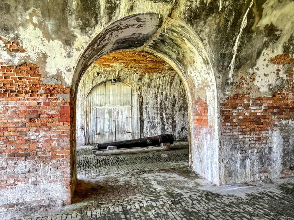 Inside the inner brick wall of Fort Morgan with arched brick walkways and a cannon on the ground.