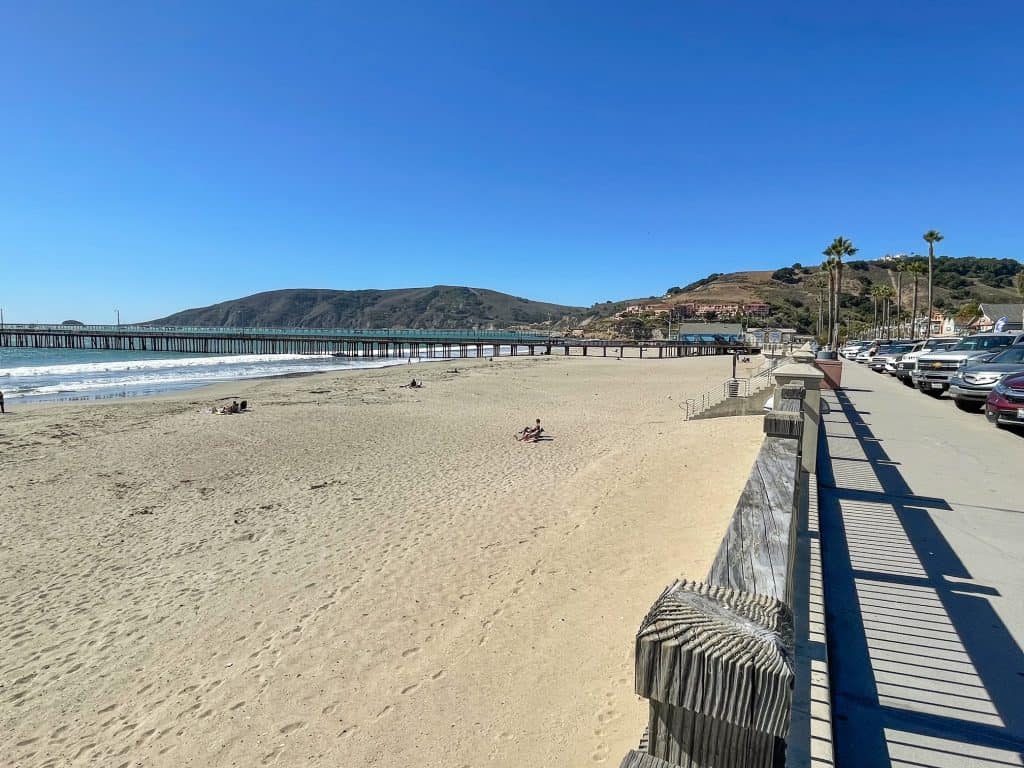 Walking along the path up above the beach with view of pier and shops in Avila Beach.