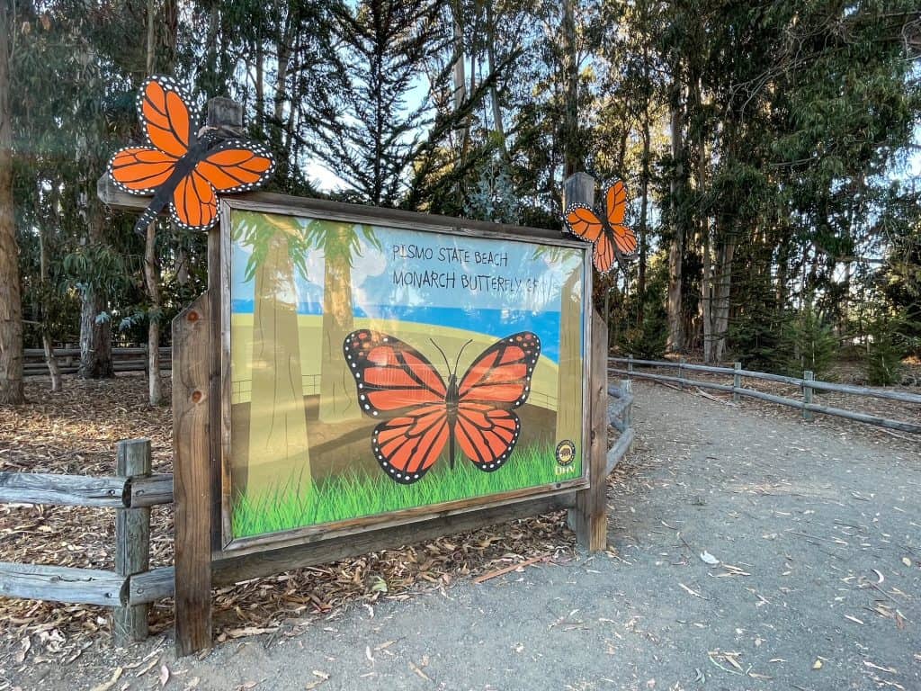 A large sign welcoming visitors to the Monarch Butterfly Grove with big pictures of the orange and black Monarchs.
