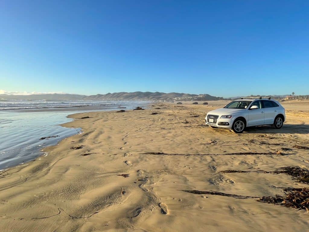 A white SUV parked on the sand at Pismo Beach steps away from the shoreline.