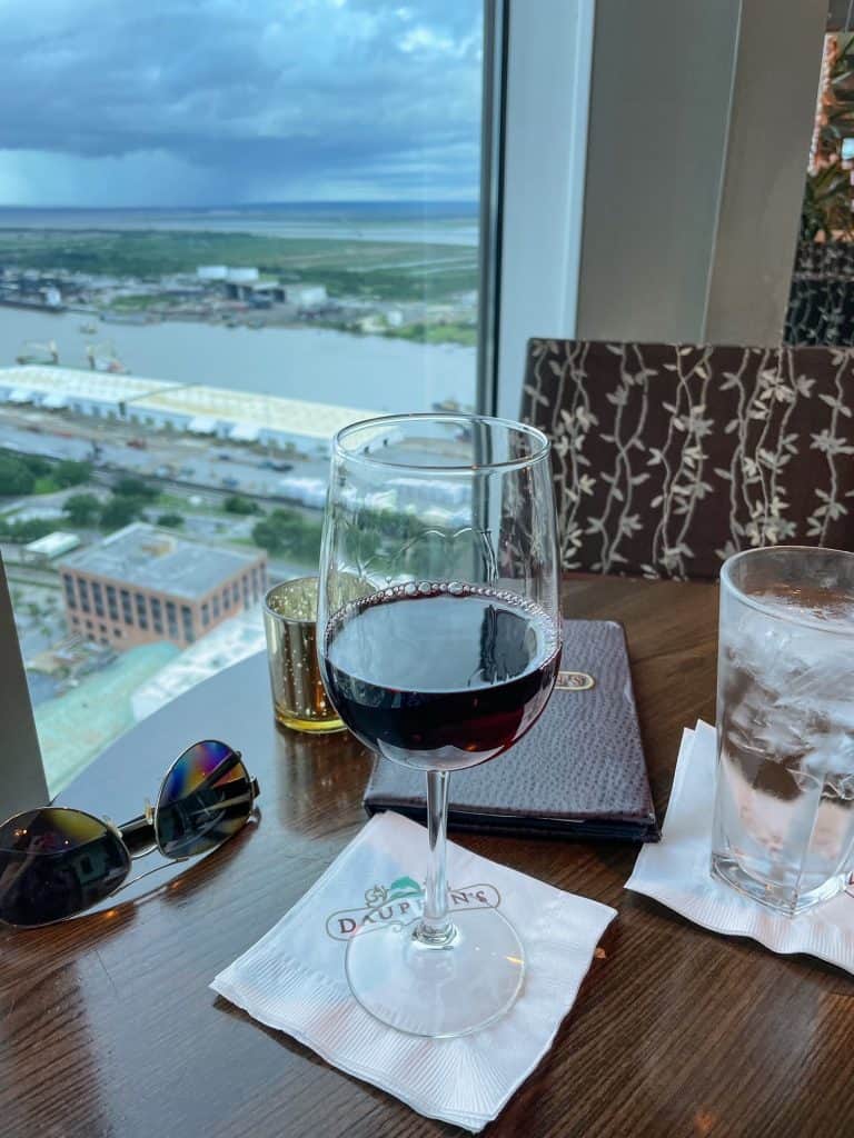A glass of red wine with the view of the Mobile River and city below looking out.