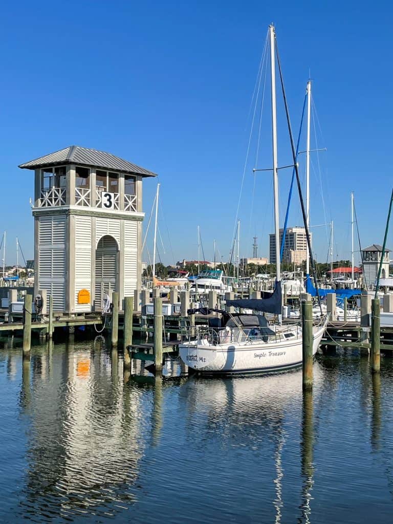 A beautiful sailboat docked at the marina with a tower on boardwalk next to it.