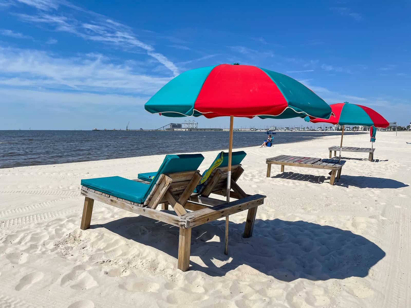 A green and red beach lounger and umbrella on the white-sand Gulfport Beach in Mississippi.