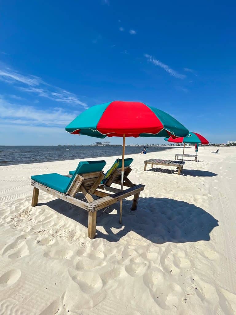 A row of red and green umbrella and beach loungers on the white sand beach of Gulfport, MS.