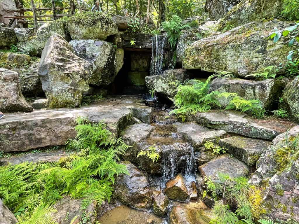 A lovely waterfall cascading down over the entrance to the cave among boulders and ferns at Garvan Woodland Gardens in Hot Springs.