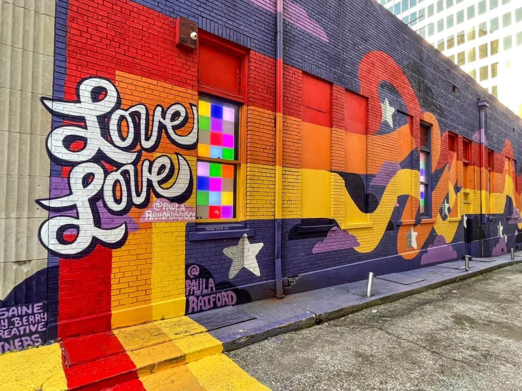 A colorful and pretty art mural on side of building with words "love, love" in red, orange, yellow, and purple colors.