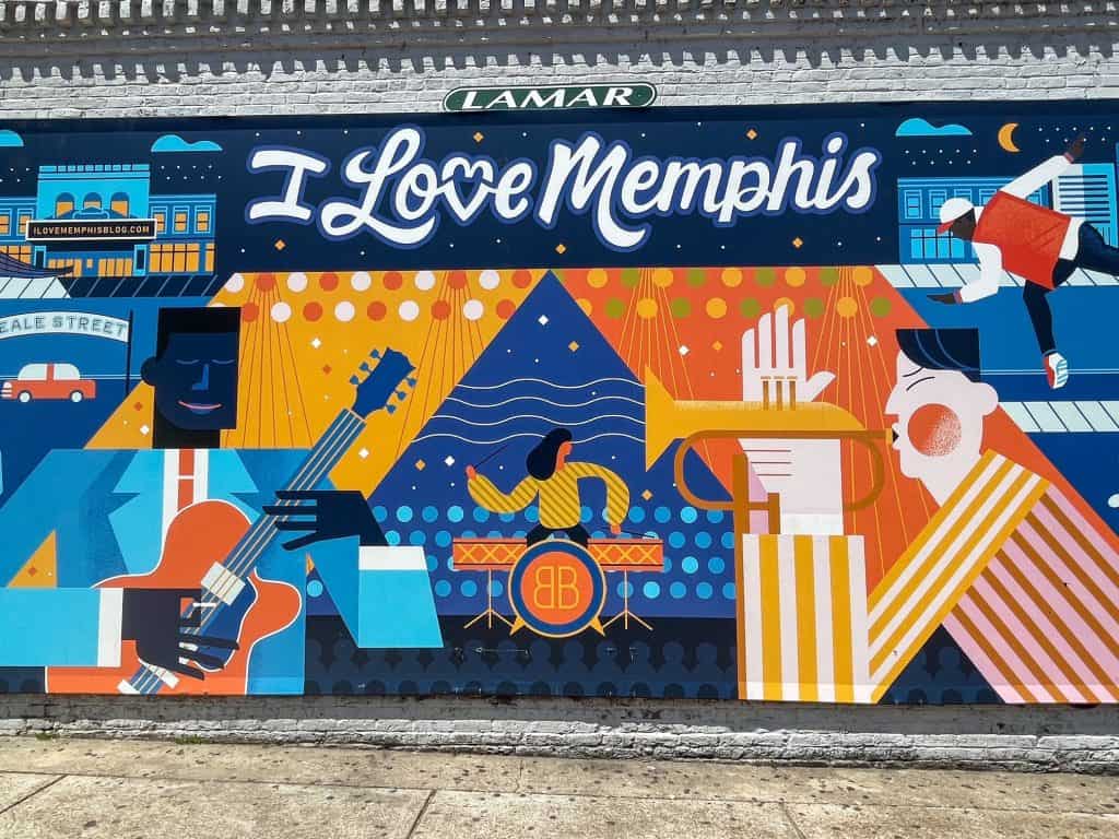 A bright and fun art mural on Beale Street with men and woman playing in a band playing drums, guitar, and trumpet with words I Love Memphis, one of many art murals to see on a weekend in Memphis, Tennessee.