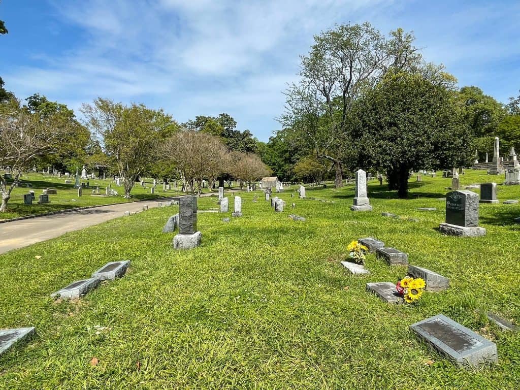 Looking out over a section of Elmwood Cemetery with beautiful green grass, trees, and headstones throughout.