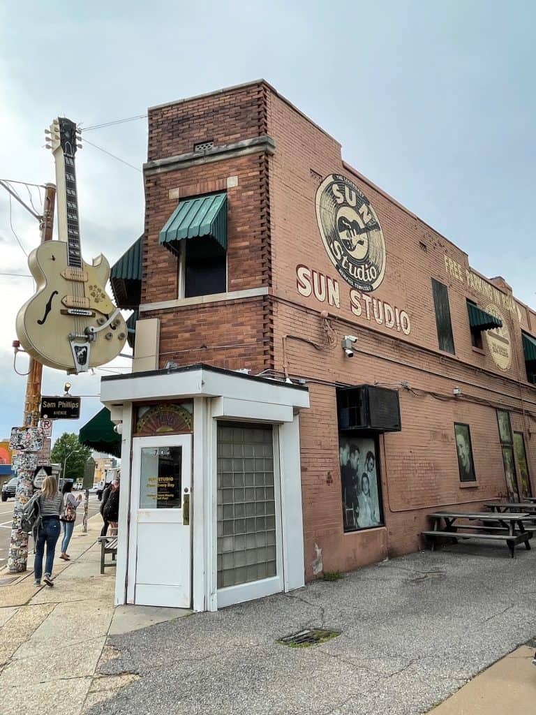 The front view of the old Sun Studio building in red brick, a white door, and a huge guitar hanging out front in Memphis, TN.