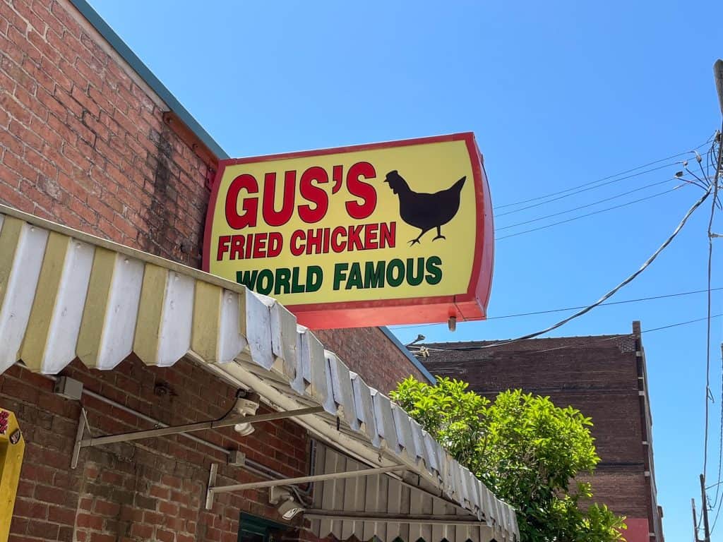 The yellow, red and black sign out front of Gus's Fried Chicken with a chicken on it.
