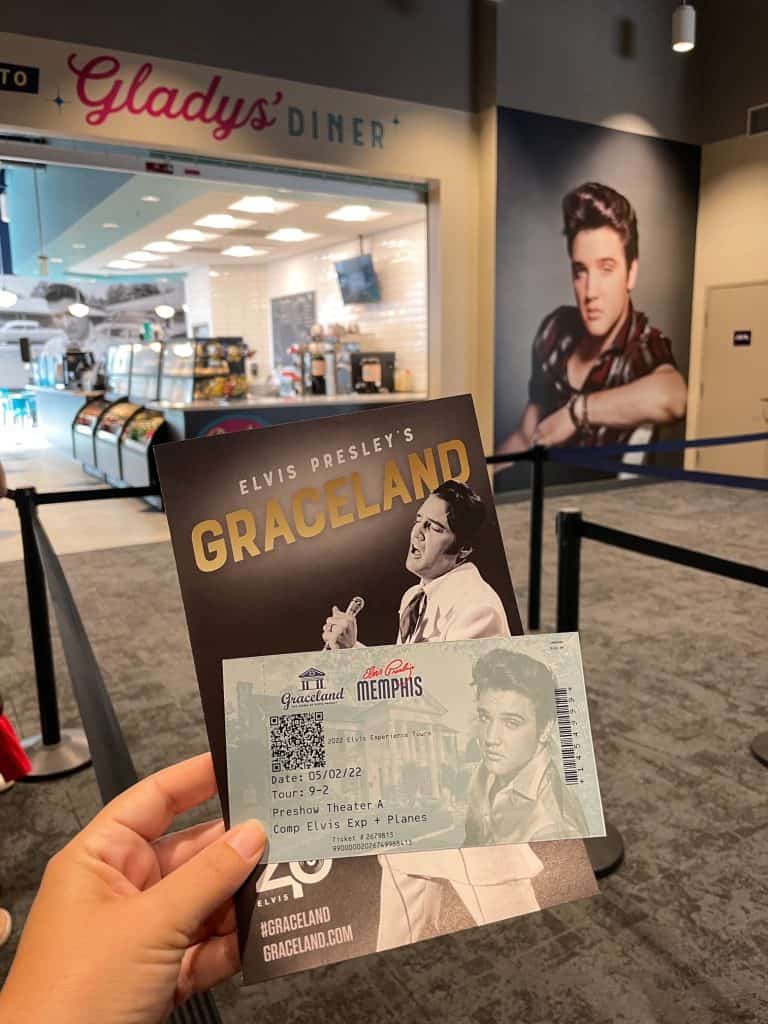 Holding up a ticket and map for Graceland with a picture of Elvis in the background waiting to get on the shuttle in Memphis, TN.