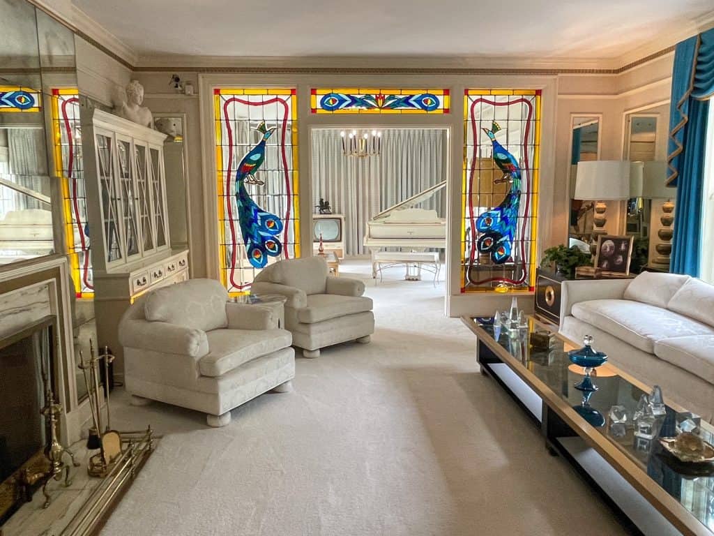 The all white furniture and carpet in the living room with yellow and turquoise stained glass and a white piano in the back at Elvis Presley's mansion at Graceland.