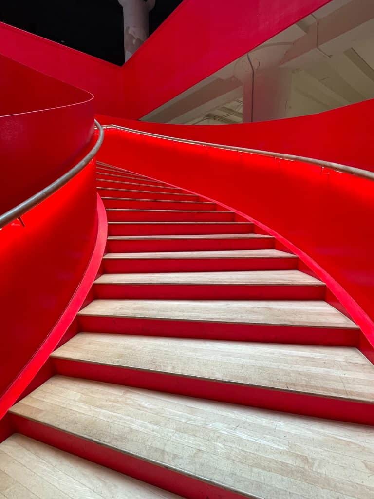 A beautiful spiral staircase with light wood steps and vibrant red panels on the side in Crosstown Concourse that used to be a Sears-Roebuck building in Memphis.