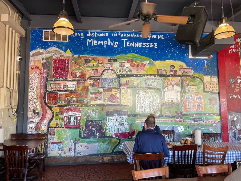 An entire wall inside of Central BBQ that has a mural of downtown Memphis area in bright colors.